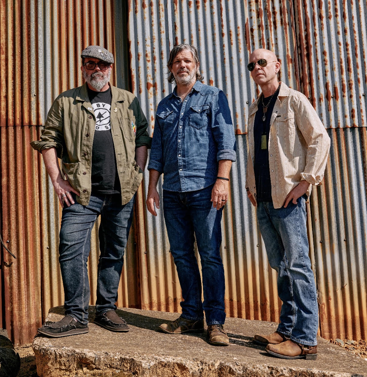 The three members of Revelwood Mission beside a corrugated metal wall